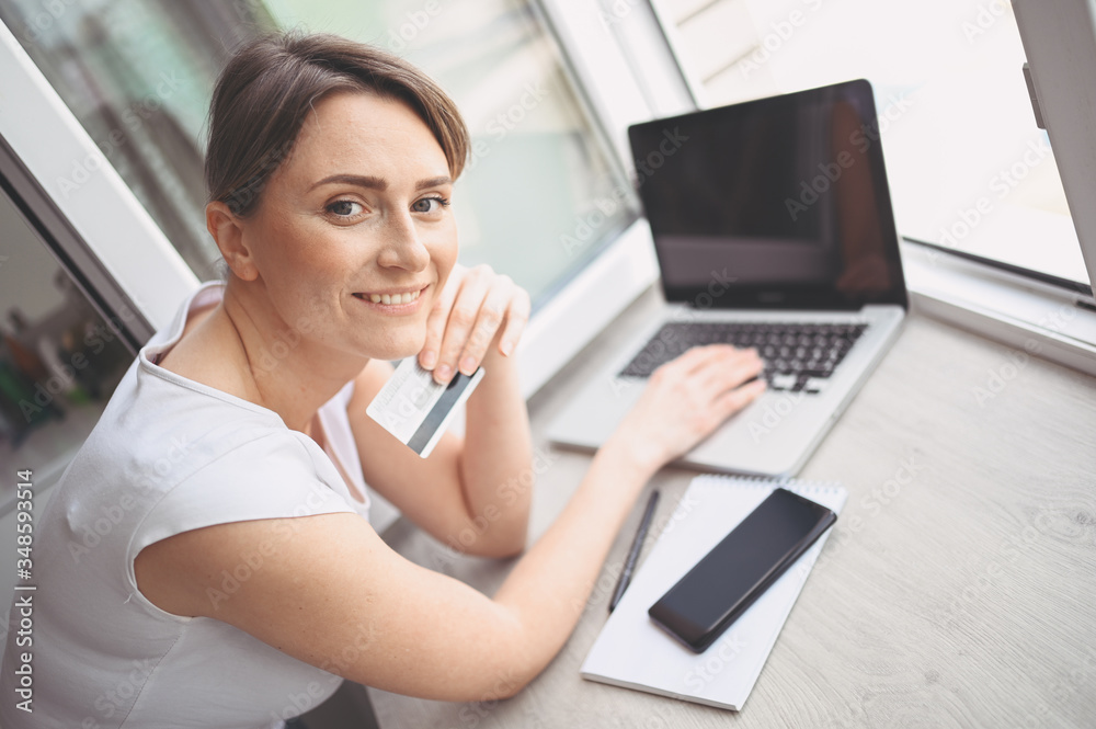 Beautiful happy woman holding credit card in hand and using laptop computer keyboard. Businesswoman or entrepreneur working. Online shopping, e-commerce, internet banking, spending money concept Beautiful happy woman holding credit card in hand and using laptop computer keyboard. Businesswoman or entrepreneur working. Online shopping, e-commerce, internet banking, spending money concept