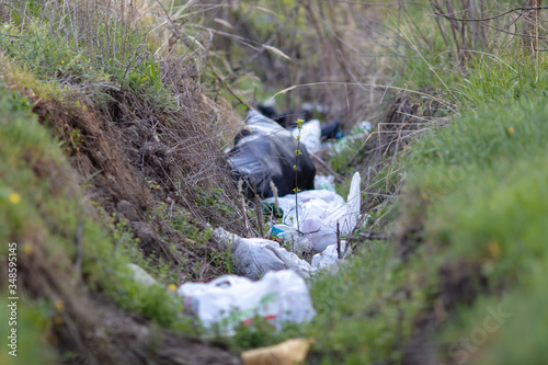 The trench overgrown with green grass and thrown with garbage and plastic bags.
