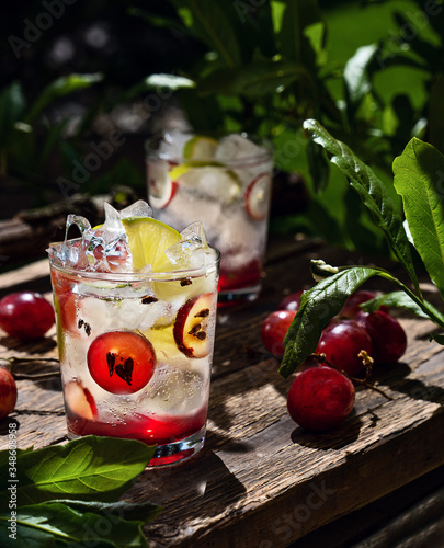 Non-alcoholic grape-lime lemonade with ice in glasses  on the wooden board in the summertime garden.