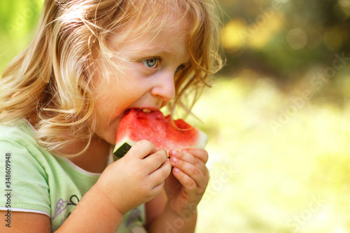 cute little girl eating a piece of watermelon close in the garden in summertime