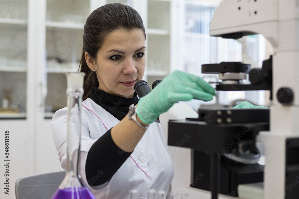 Working with a microscope in a research laboratory. A female chemist works with a microscope.