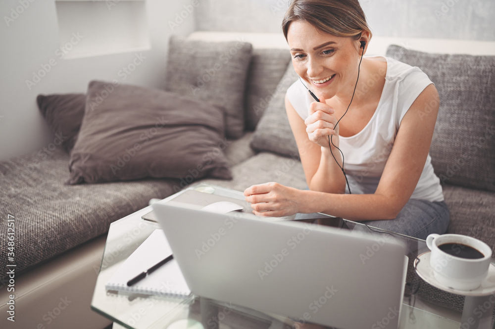 Attractive happy young student studying online at home, using laptop computer, headphones, having video chat, waving. Remote work, distance education. Video conference or virtual event on quarantine