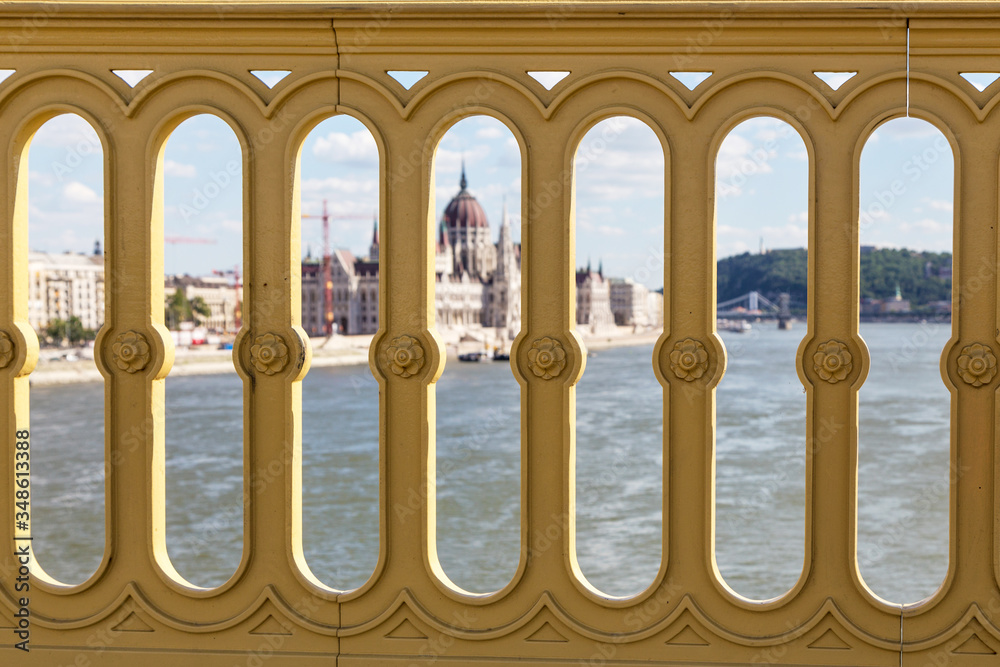 Fototapeta premium View of the building of the Hungarian Parliament and the Danube River through the fence of the bridge. Budapest, Hungary. Sunny summer day.