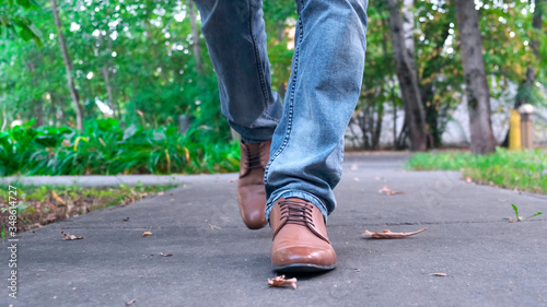 View of man s walking legs in blue jeans  brown leather shoes.