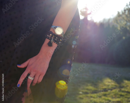 Kobieta z zegarkiem w czarnej sukience oświetlana słońcem