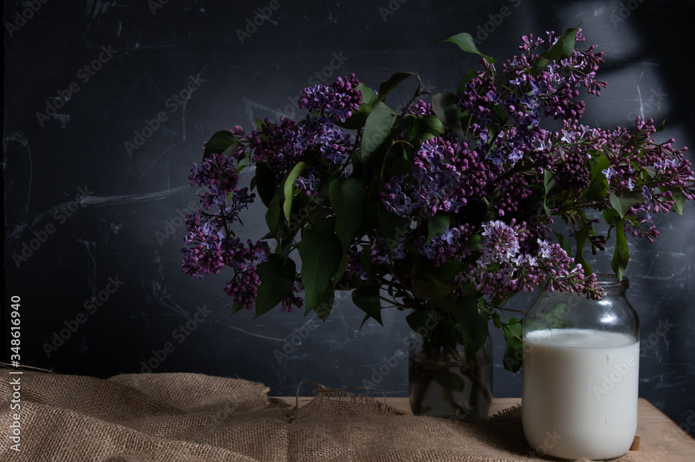 Fresh milk in a pot and a bouquet of flowers. Rural still life with