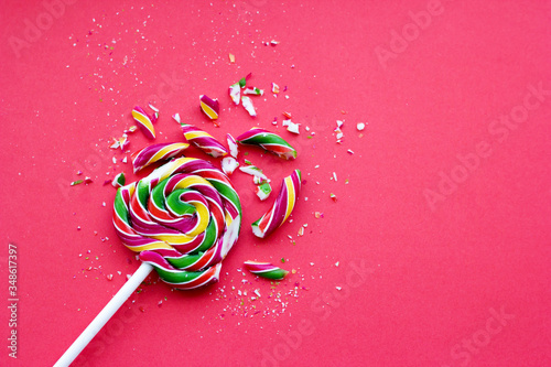 Broken in pieces candy on a stick. Smashed lollipop on pink background, top view with copy space. photo