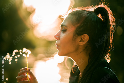 Valokuvatapetti Young beautiful woman blowing dandelion at sunset