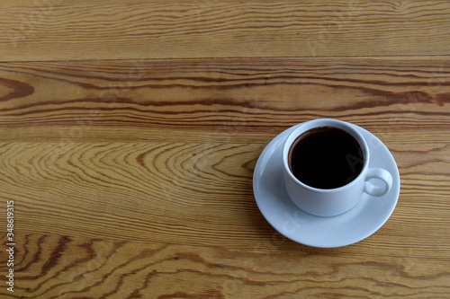 The white cup of coffee is on a wooden beige surface.