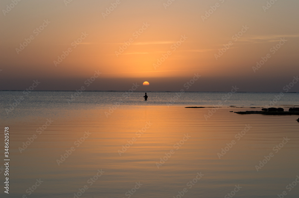 夕日のオレンジ色が反射した穏やかな海で釣りをする人