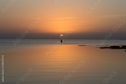 夕日のオレンジ色が反射した穏やかな海で釣りをする人 © Ta-c