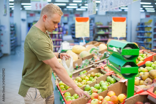 Young sporty man is choosing fruits in grocery store. Concept of healthy nutrition, balanced diet, vitamins