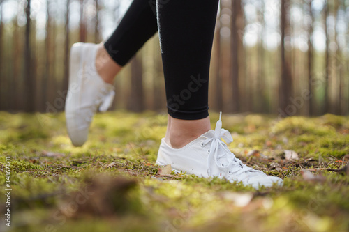 Runner feet running on road closeup on shoe. Jogging on a path in a pine forest. Woman running. White women's sneakers. Healthy lifestyle and weight loss concept.