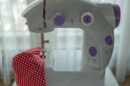 Face mask sewing: Mini sewing machine with a red fabric face mask. DIY craft during coronavirus disease situation.