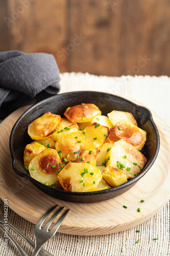 Roasted potatoes slices in iron skillet with herbs. Rustic background, copy space, selective focus. Homemade food. Nutrition concept.