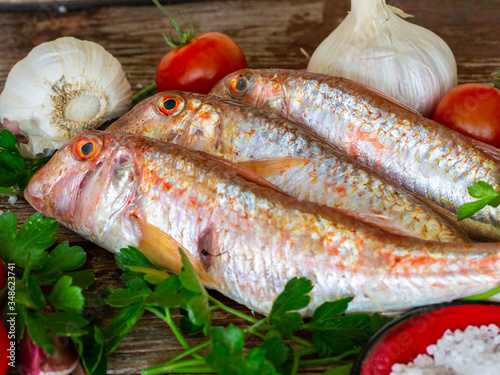 red mullet on an old wooden board background with typical ingredients of an Italian recipe "triglie alla livornese"