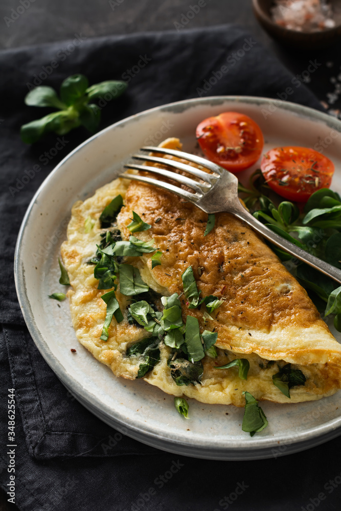 Stuffed omelette with tomatoes, red bell pepper, cream cheese and corn or lamb's lettuce on dark wooden background with copy space. Healthy diet food for breakfast. Selective focus.