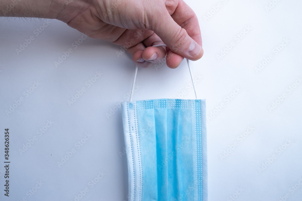 a man's hand holds a blue disposable medical mask on a white background close up