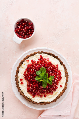 Homemade dessert chocolate tart with coconut cream and pomegranate and mint on a pink table background. Top view.