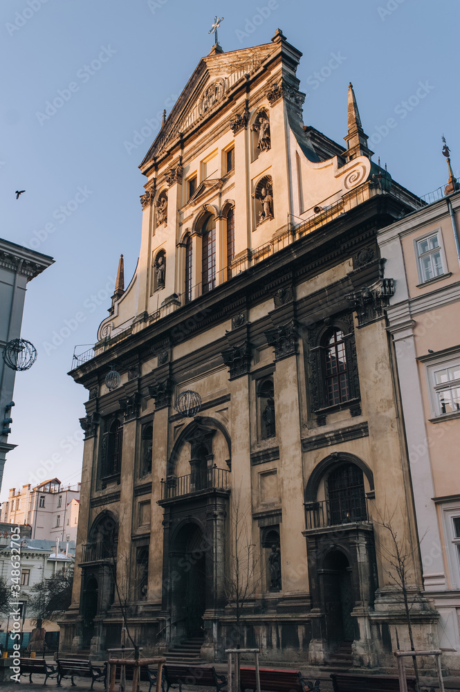 Jesuit Church in Lviv. Antique baroque facade with windows by decorative stucco on a beige wall with capitals and with sculptures of the Holy Fathers and the Blessed Virgin Mary in niches.