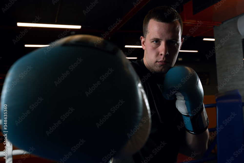A young boxer in blue gloves in the ring in the gym looks into the camera. Getting ready for impact
