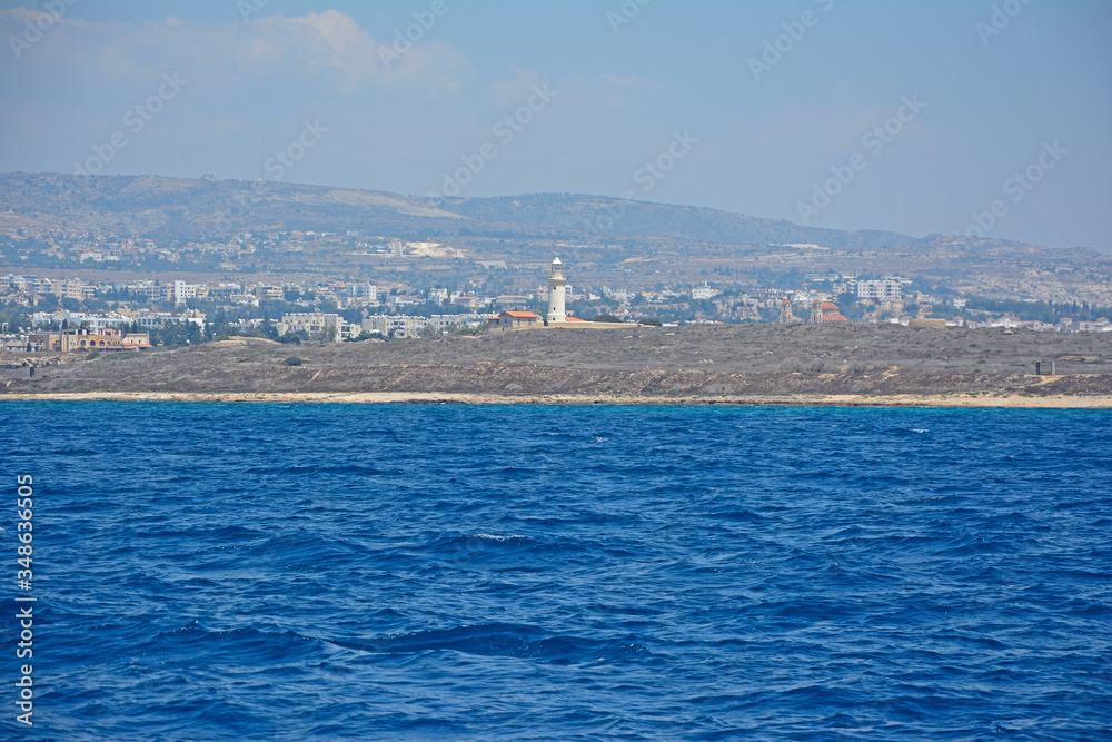 The picturesque coast of the Mediterranean sea with houses on the shore in the distance and an ancient lighthouse