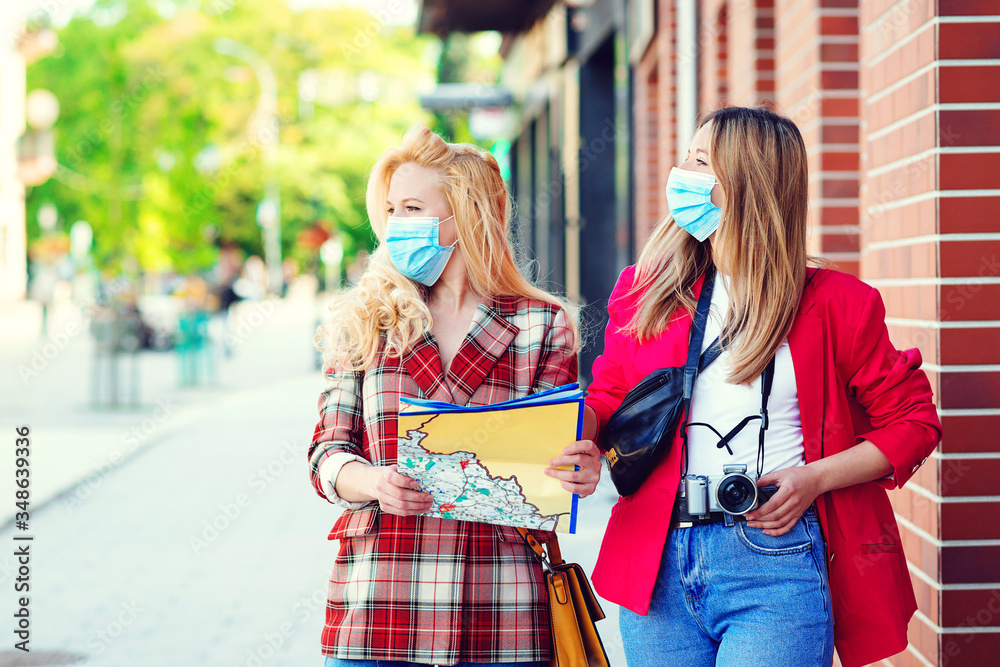 Student girls are exploring new city together. Summer vacation during coronavirus pandemic. Tourists in medical masked.