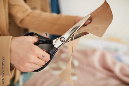 Close-up of tailor holding piece of fabric in her hands and cutting it with scissors