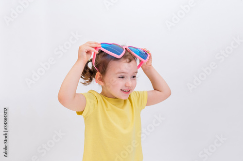 A little blonde girl held up big funny glasses on a white background. Day of laughter. Children's game.