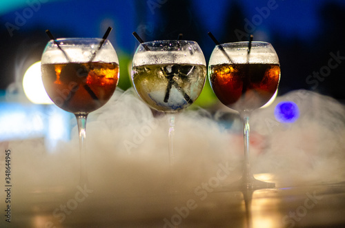 Beautiful row line of different colored alcohol cocktails on a party, martini, vodka,and others on decorated catering bouquet table on open air event, picture with beautiful bokeh