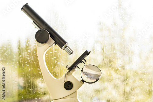 Сoncept of careful observation of the weather. Prediction of rain, thunderstorms. Microscope on the background of a window with drops.