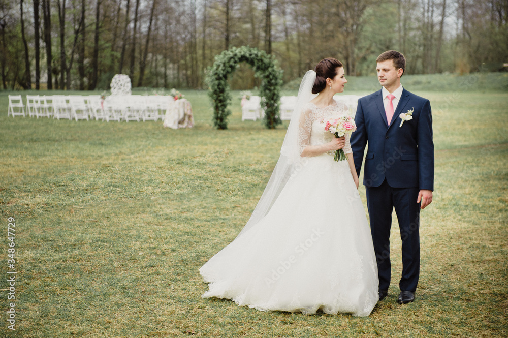 Wedding in the spring. Ceremony outside. An arch of real flowers. The bride and groom look at each other.