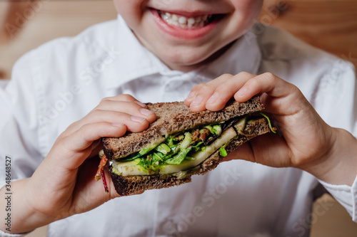 Фотография close up, child with vegetarian sandwich with whole grain bread, cucumber, egg whites, radishes and pea shoots on plate