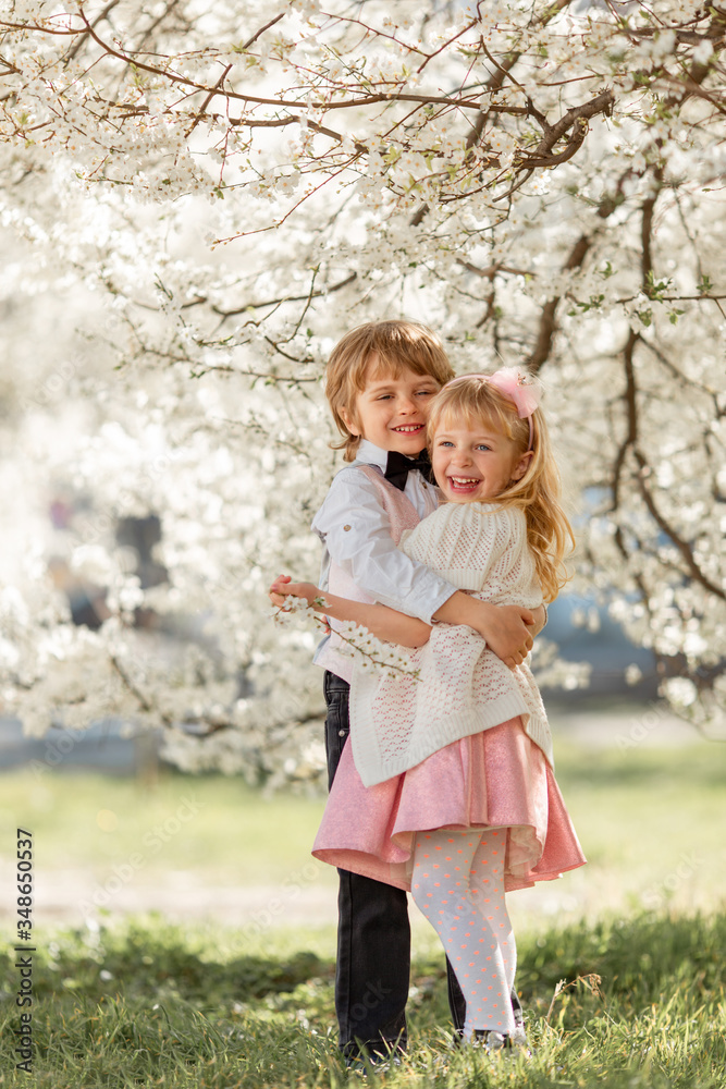 Happy sister and brother are playing in blossom cherry garden outdoors. Happy sister and brother are playing in blossom cherry garden outdoors.