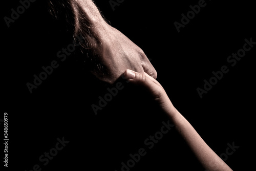 Adult and child holding hands on black background adult hand supporting child