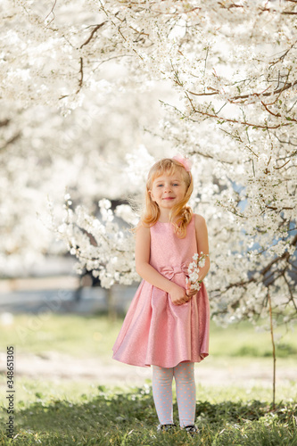 Cute little child girl is playing in blossom cherry garden outdoors. © _chupacabra_