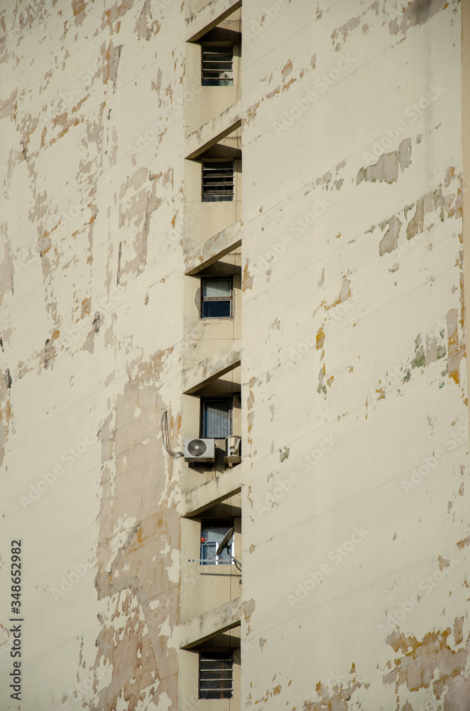 close up on a beige facade with a few windows and peeled paint