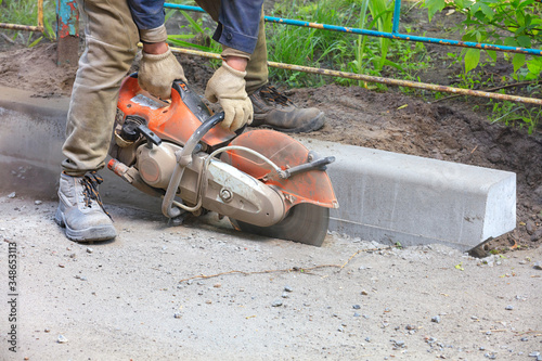 A construction worker using a concrete saw cuts asphalt and concrete curbs to create a track.