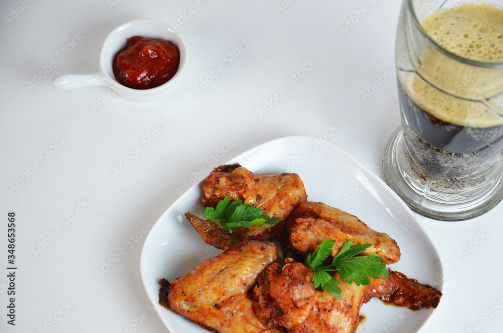buffalo chicken wings barbecue or grill with red sauce in a gravy boat, beer in a tall glass with foam on a white background