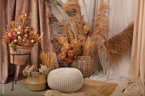 Home cozy interior of room in brown tones with dried flowers, pampas grass and branches in basket. Scandinavian design. Rustic. Boho. Dry flowers in pot in elegant room interior with natural accents	
