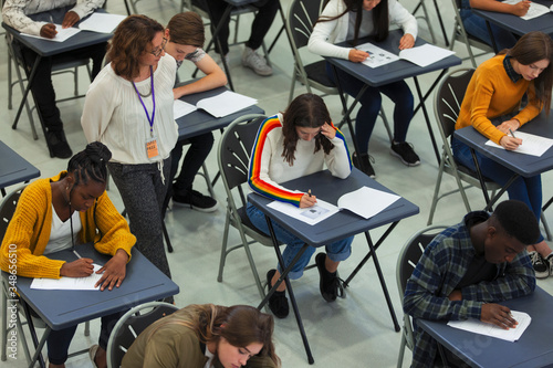 High school teacher supervising students taking exam at tables photo
