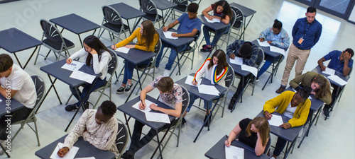 Instructor supervising high school students taking exam at desks photo