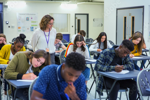 High school teacher supervising students taking exam at desks photo