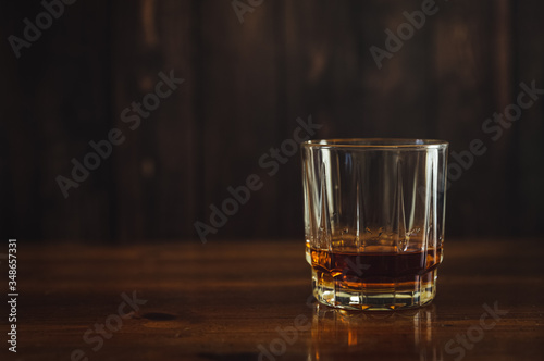 Whiskey or scotch neat in a glass resting on a wood table.