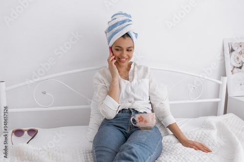 Cute pretty girl is wearing towel on her head talking phone with friends. Beauty and stay home concept.