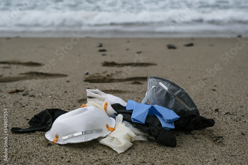 Protective virus mask and plastic gloves medical waste on sandy sea shore,coronavirus covid pollution disease 