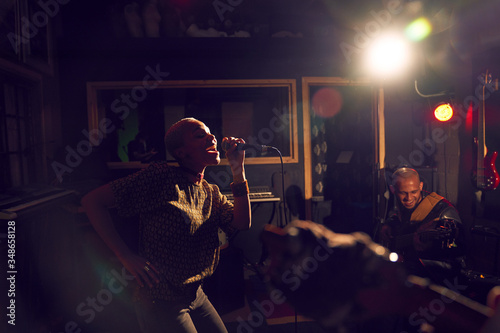 Female musician singing into microphone in dark recording studio photo