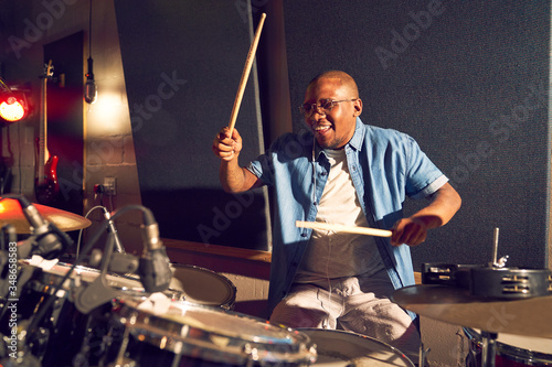 Smiling young male drummer playing drums in recording studio