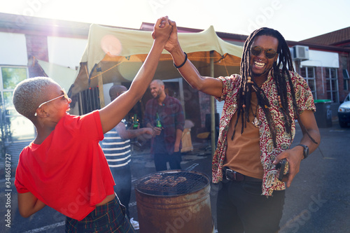 Happy friends high fiving and barbecuing in sunny parking lot