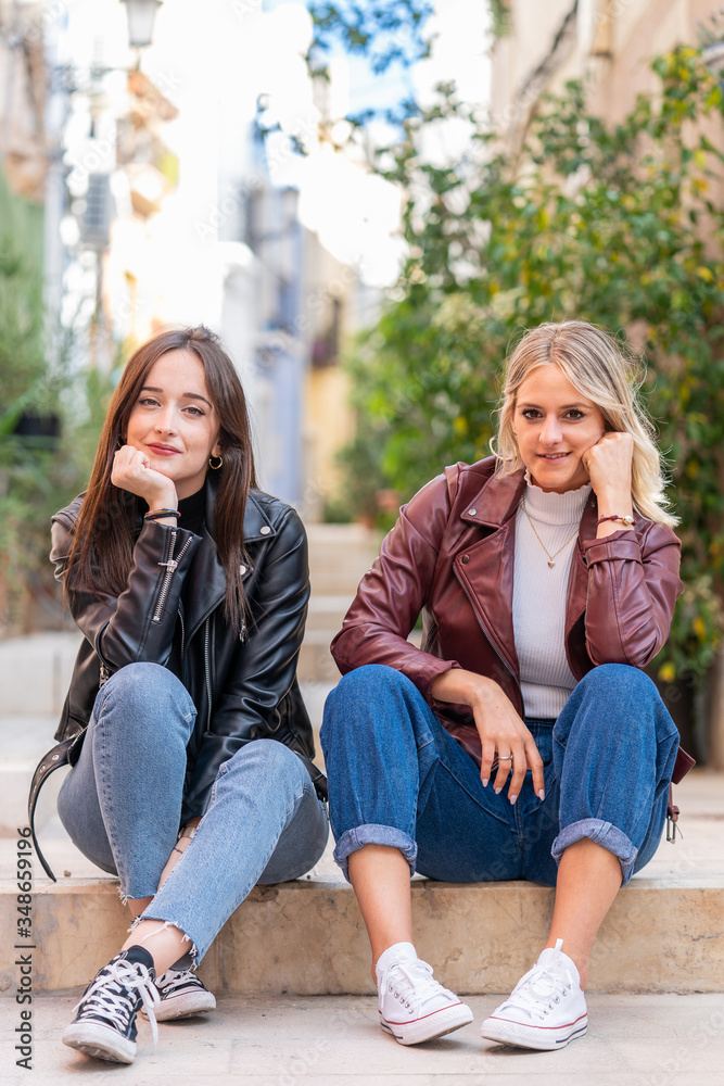 couple of attractive girls sitting on the street dressed in casual clothes.